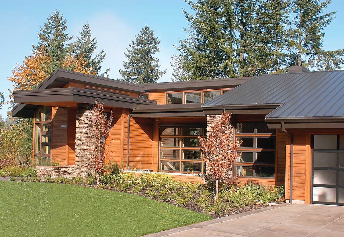 Modern house plan exterior with wood siding, stone accents, deep eaves, and metal roof. Features expansive windows and a glass garage door.