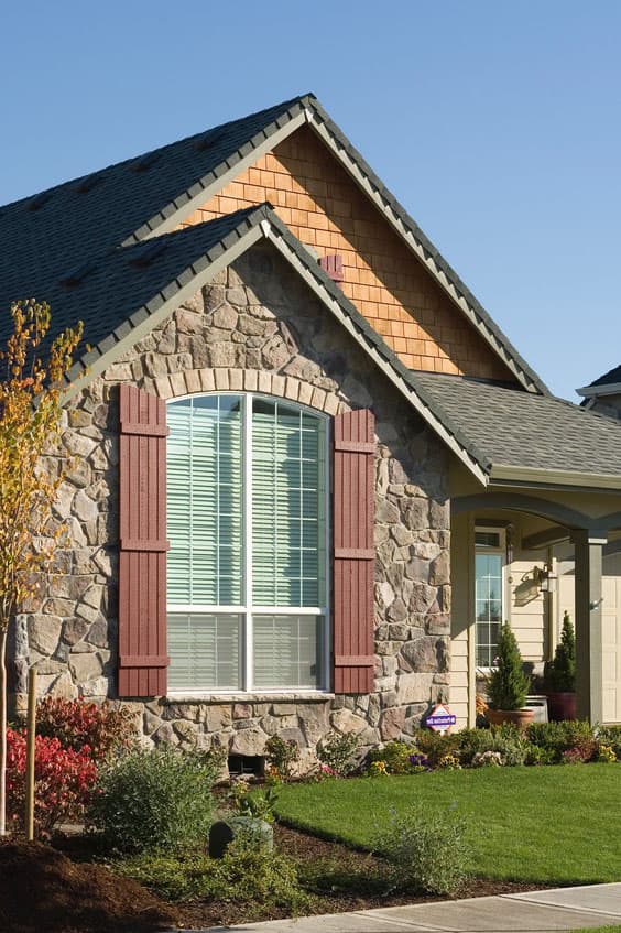 House plan exterior featuring stone facade, arched window with red shutters, and wood shingle gable.