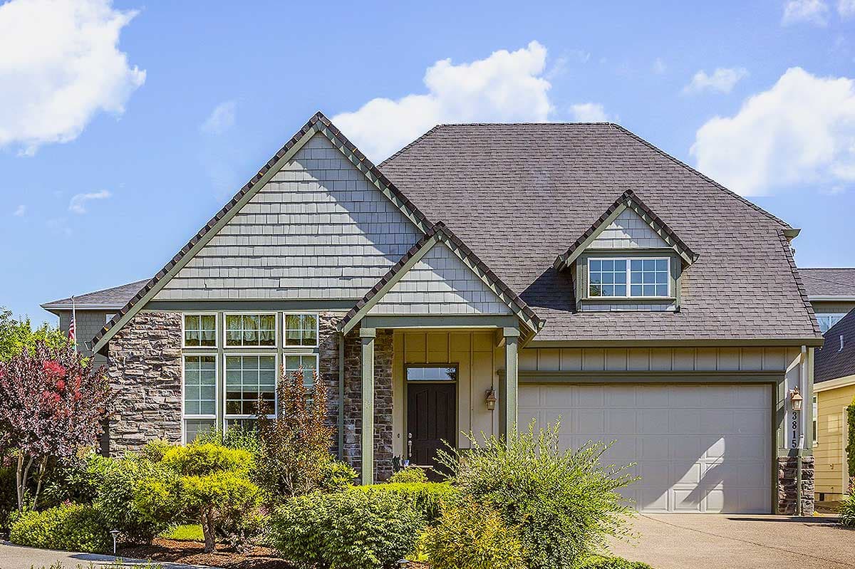 House plan exterior. Two-story Craftsman with a gabled roof, stone facade, and dormer window above the garage.