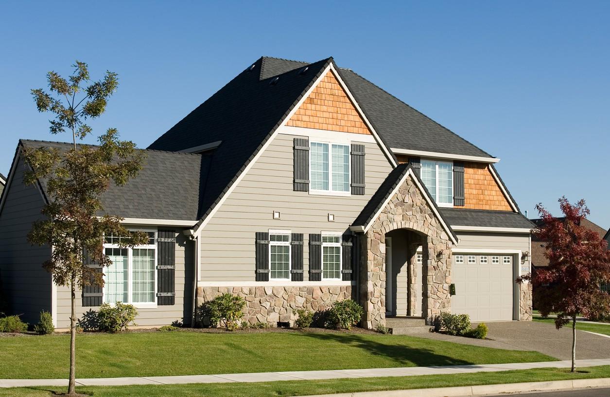 House plan exterior: Two-story home with stone arched entry, gabled dormers, wood shingle accents, and side-facing garage.