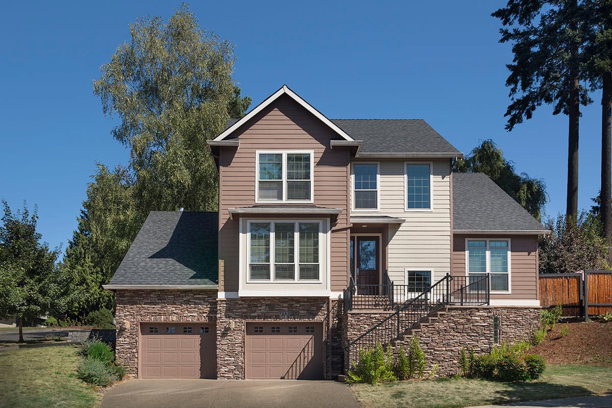 House plan exterior. Two-story home with a gabled roof, stone veneer foundation, and a two-car garage. Features multiple dormers and a front entrance.
