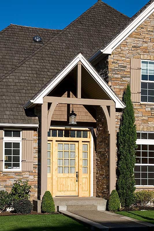 House plan exterior: wood-shingled roof, stone facade, arched entryway with wooden double doors and multiple panes.