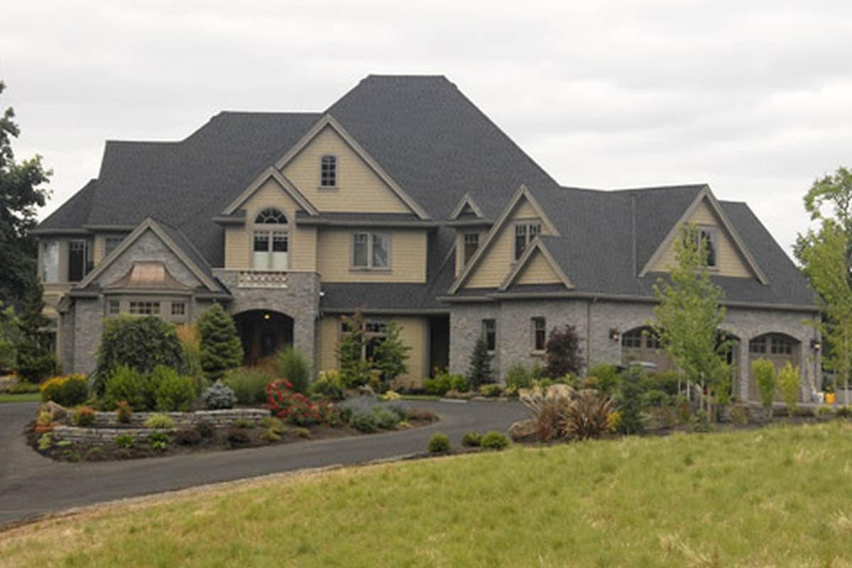 House plan exterior view of a two-story home with a gray stone facade, gables, arched entryway, and a three-car garage.