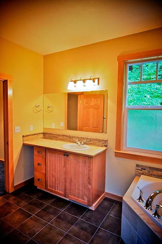 Bathroom with wood vanity, sink, mirror, and tub. Features a window and dark tiled floor.