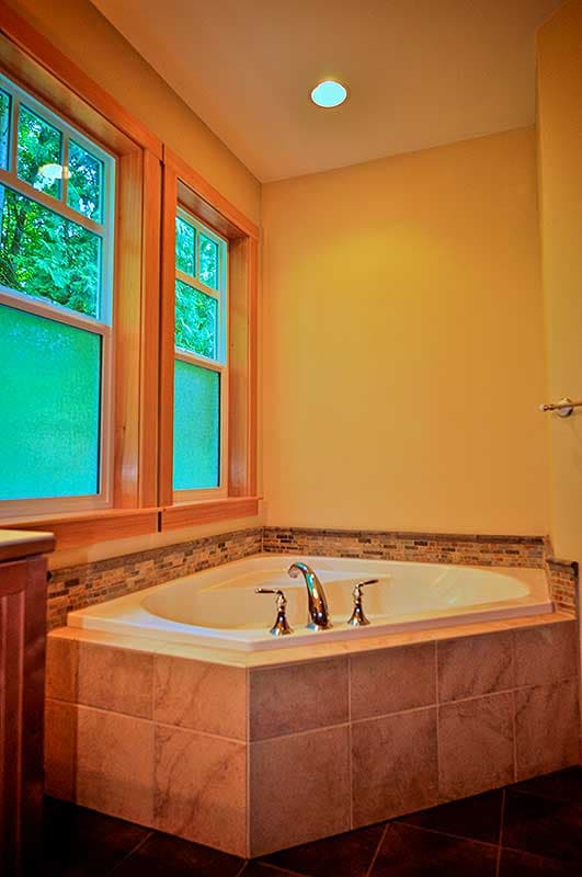 Corner soaking tub with tiled surround and windows with wooden trim.