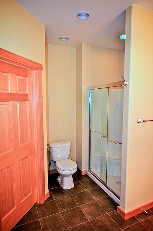 Bathroom featuring a glass-door shower stall, white toilet, and a wooden door.