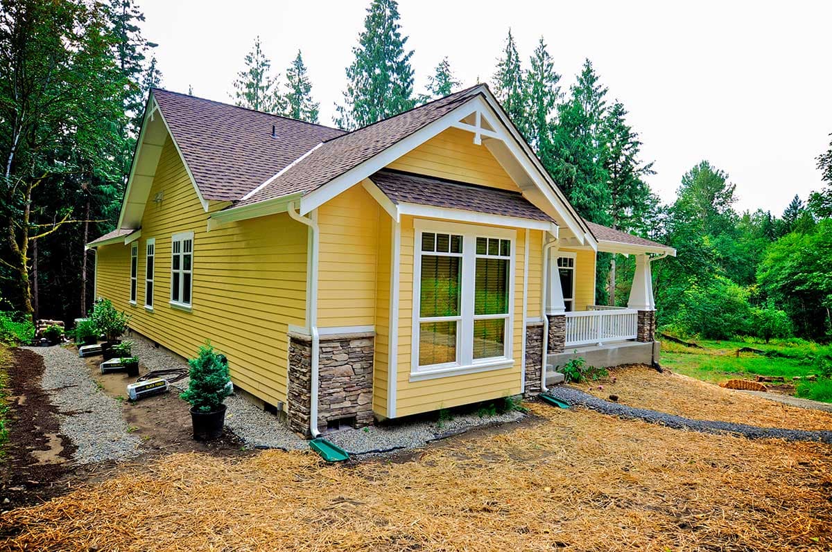 House plan exterior: Yellow siding, stone accents, gables with decorative trim, and a covered front porch with white railing.