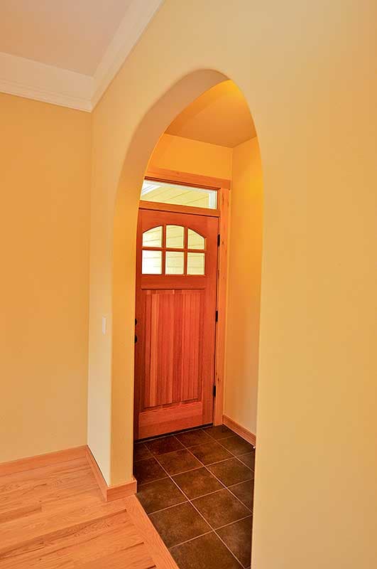 Interior view of an arched entryway with a wooden paneled door featuring a multi-pane glass transom and sidelights.