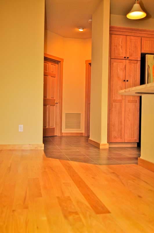 Interior view of hallway with wood doors and wood cabinetry. Tiled and hardwood floors visible.