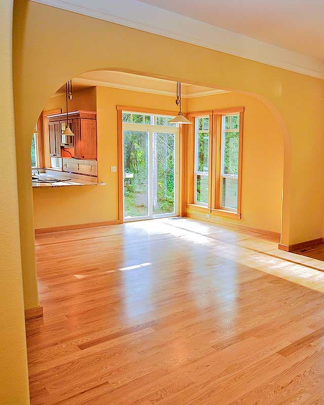 Interior view of a dining area with hardwood floors, pass-through kitchen counter, sliding glass door, and bay windows.
