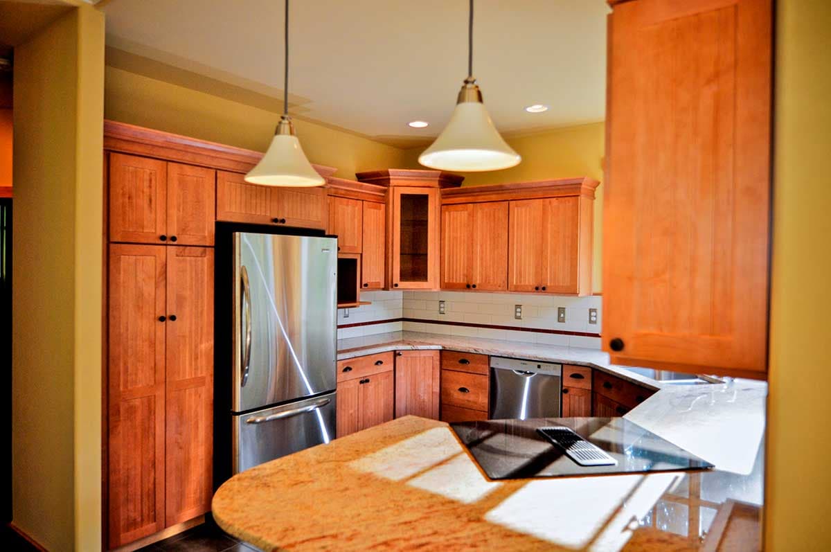 Kitchen interior with stainless steel refrigerator, wood cabinetry, granite countertop island with cooktop, and pendant lights.