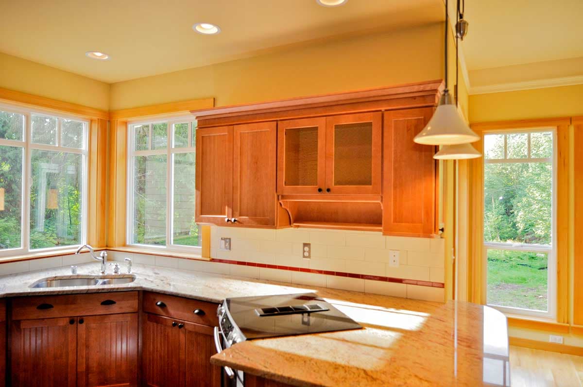 Kitchen interior with wooden cabinets, granite countertops, island, range, sink, and large windows.