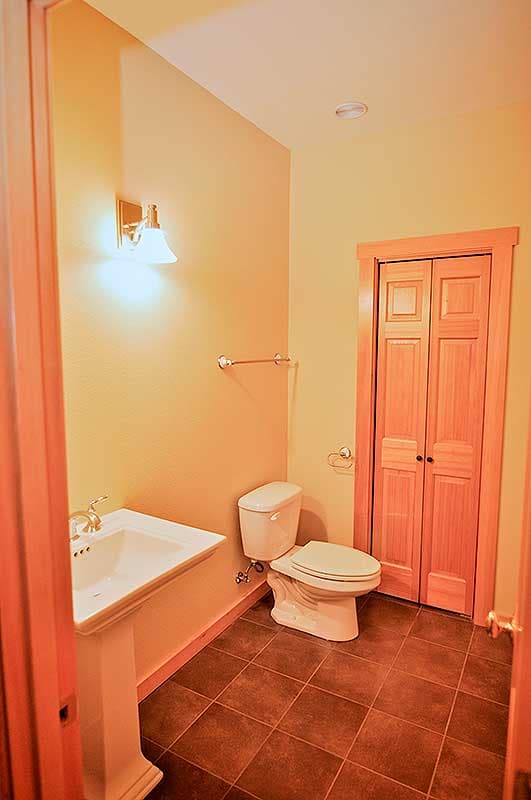 Bathroom interior with pedestal sink, toilet, wall sconce, and bi-fold closet doors.