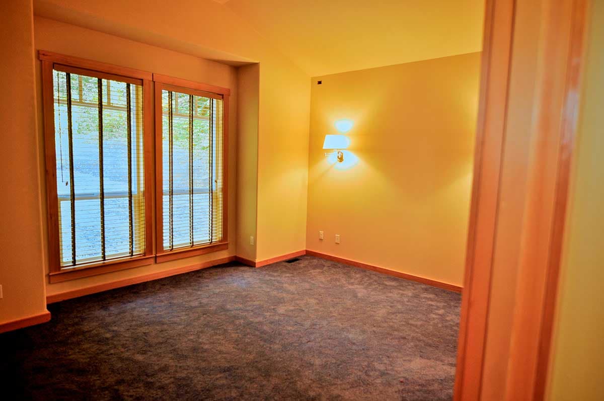 Interior view of a room with two large windows, vaulted ceiling, wall sconce, and carpeted floor.