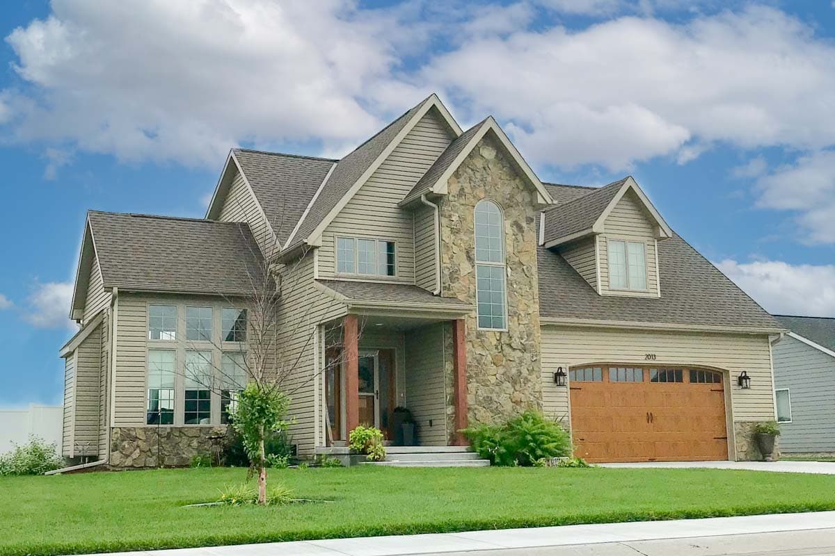 House plan exterior with two stories, Craftsman style. Features include stone facade, gabled roof, dormers, and a front-facing garage.