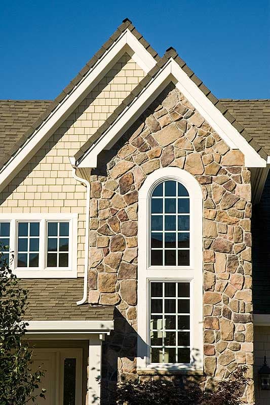 House plan exterior with stone facade, arched window, and double-hung windows under gabled rooflines.