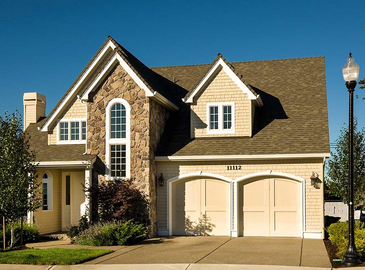 House plan exterior featuring stone accents, arched windows, shingle siding, and a two-car garage with arched doors.