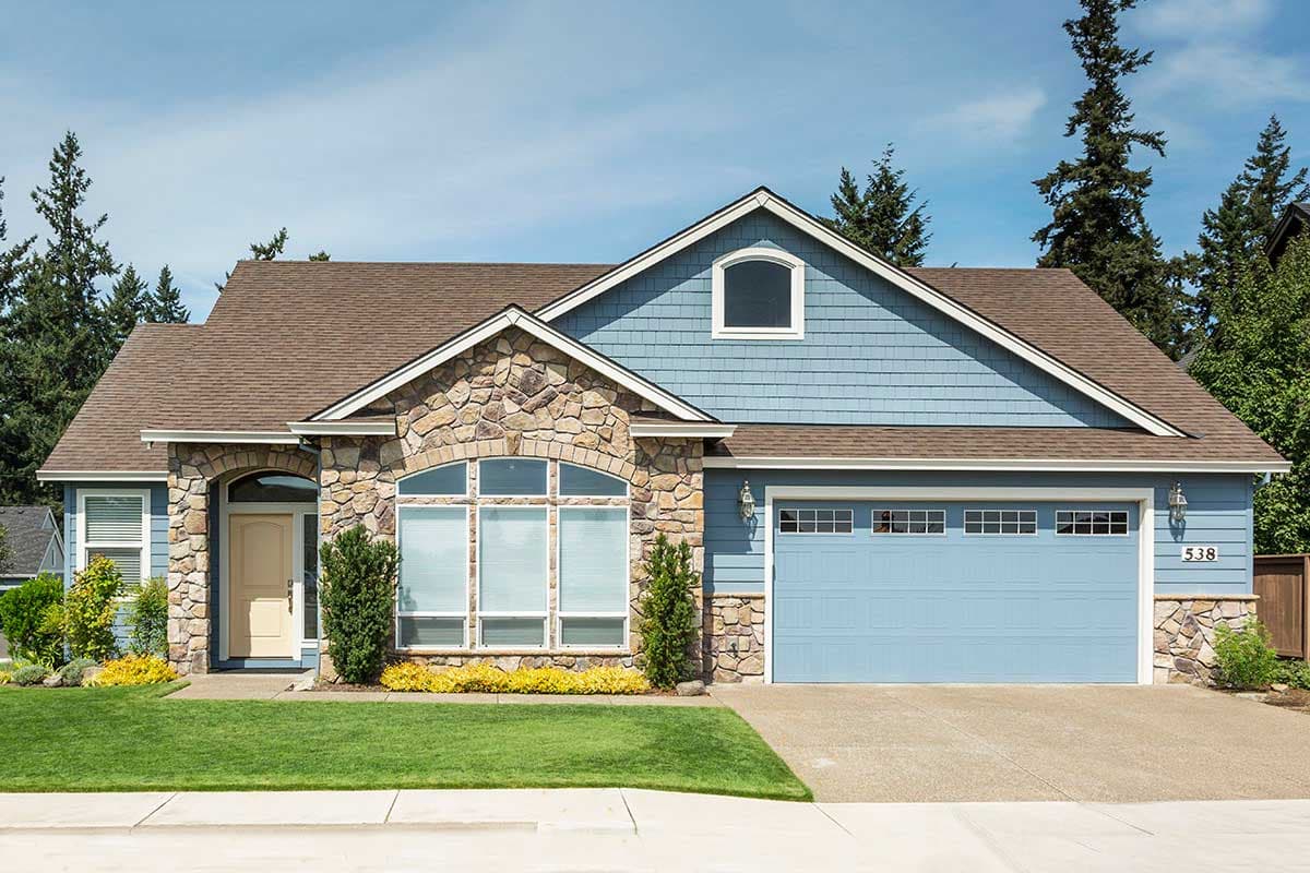 House plan exterior: Two-story home with arched stone entryway, large arched window, and blue siding. Features a dormer window and attached garage.