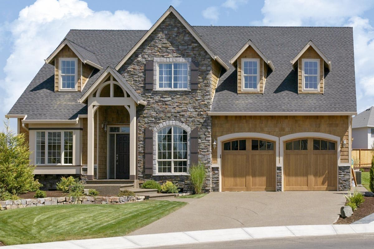 House plan exterior with stone and cedar siding, arched entry, dormers, and a three-car garage.