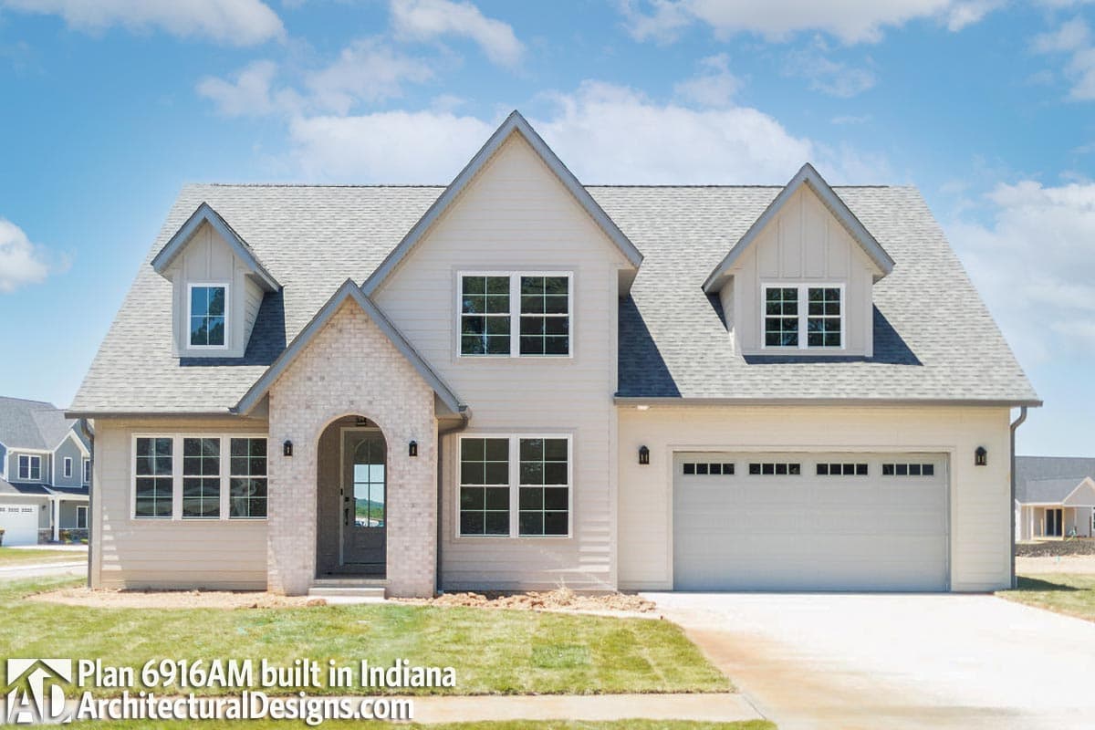 House plan exterior: Two-story modern farmhouse with gabled dormers, arched brick entryway, and side-facing garage.