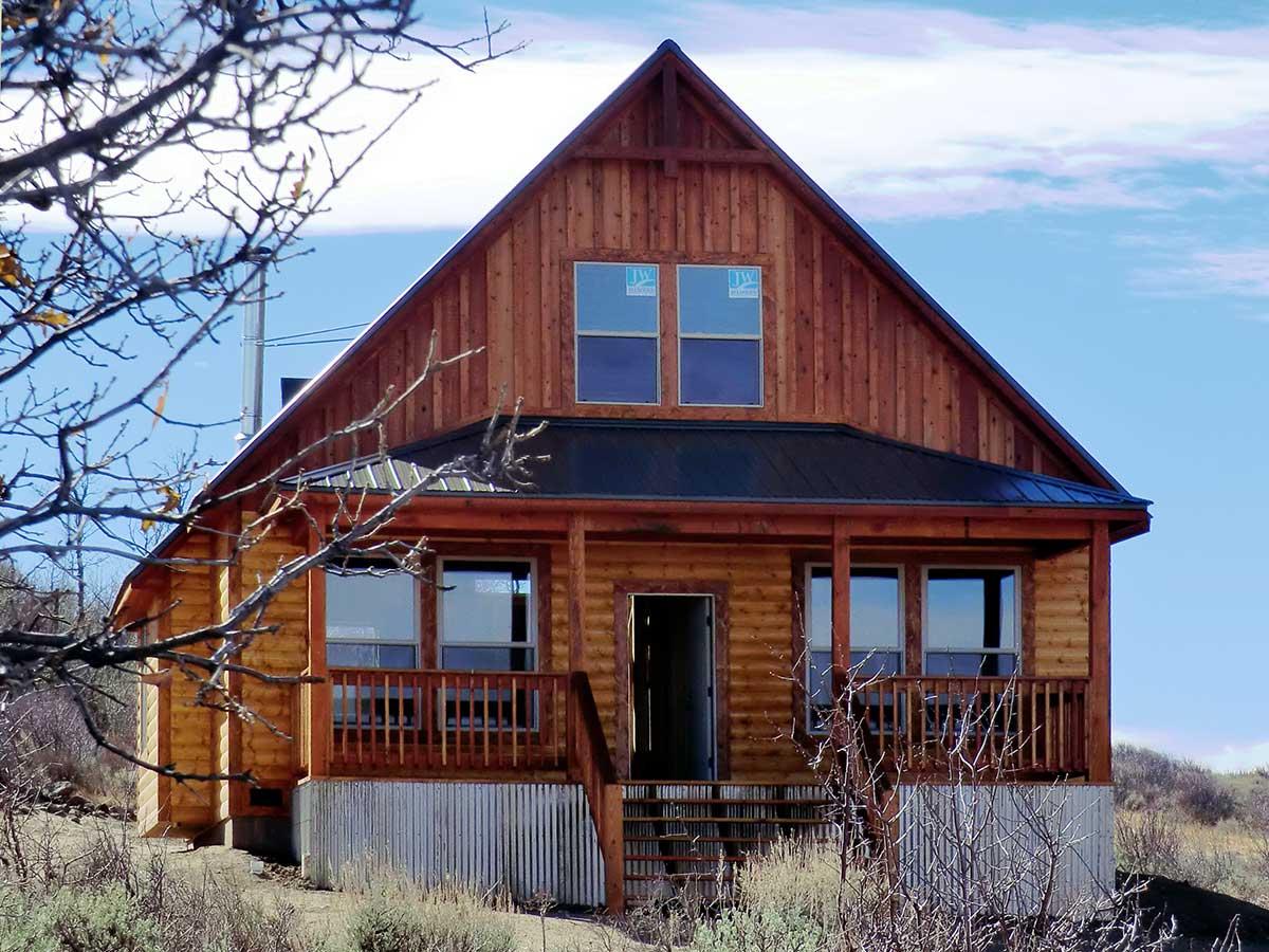 Log cabin house plan exterior with a covered front porch, metal roof, and gabled dormers.
