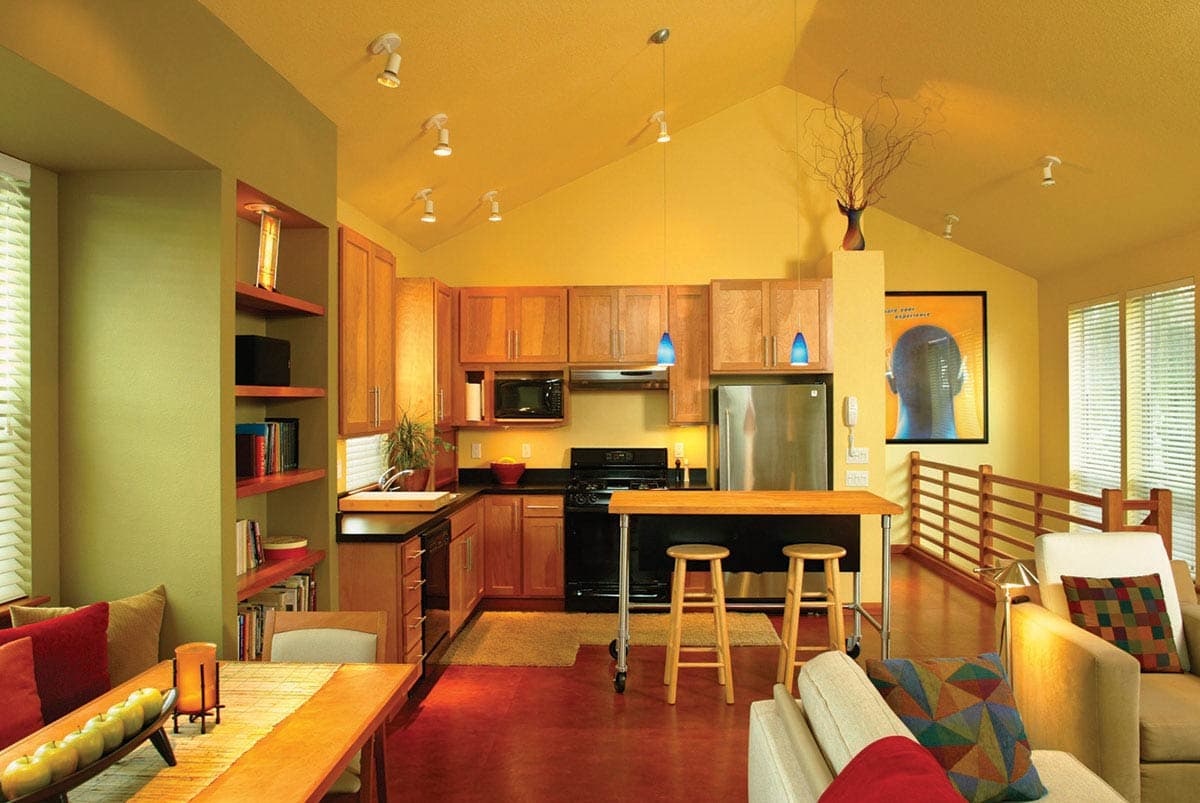 Open concept living space with vaulted ceilings featuring a kitchen, dining area, and living room with a wooden railing.