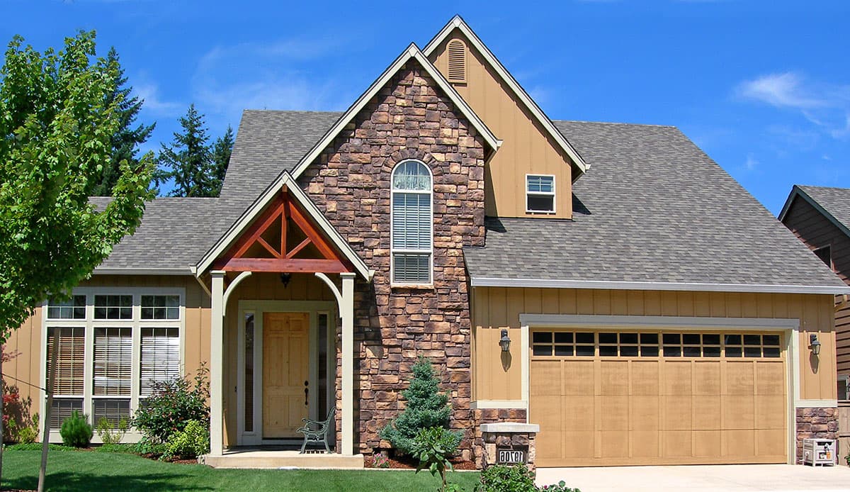 House plan exterior with stone accents, wood-shingled roof, prominent gables, and a covered entry porch.