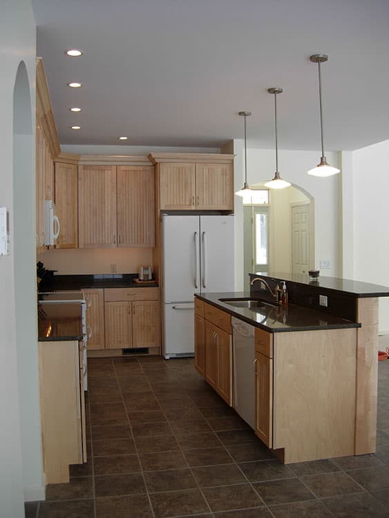 Kitchen with light wood cabinetry, granite countertops, island with sink, and stainless steel appliances.