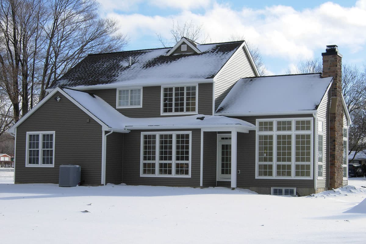 House plan exterior of a two-story home with a prominent stone chimney, multiple gables, and a large sunroom with grid windows.