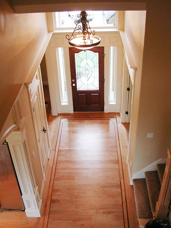 Interior view of home foyer with wood floor, stained glass front door, sidelights, and decorative chandelier.