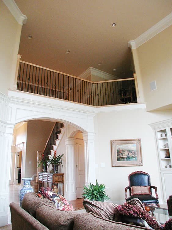 Interior view of a two-story home with a balcony overlooking the living area and a curved archway to the staircase.