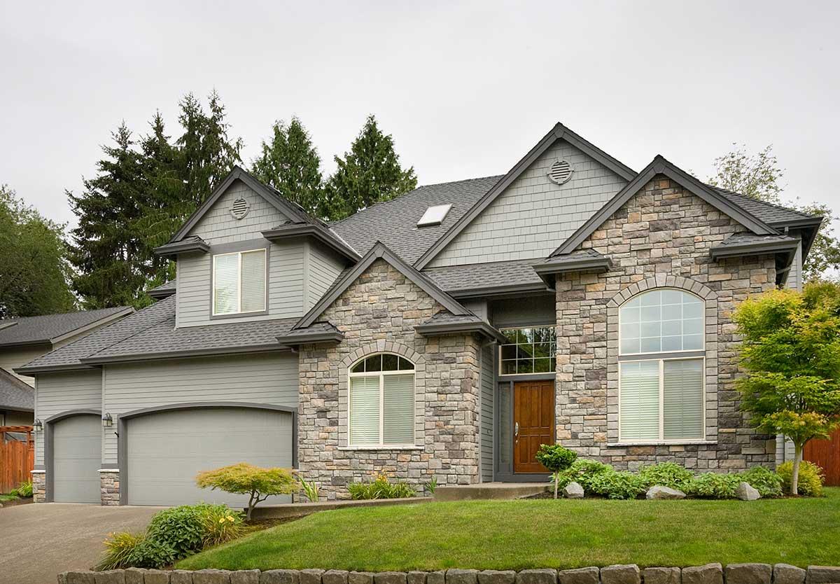 House plan exterior featuring stone accents, gabled dormers, a prominent arched window, and a three-car garage.