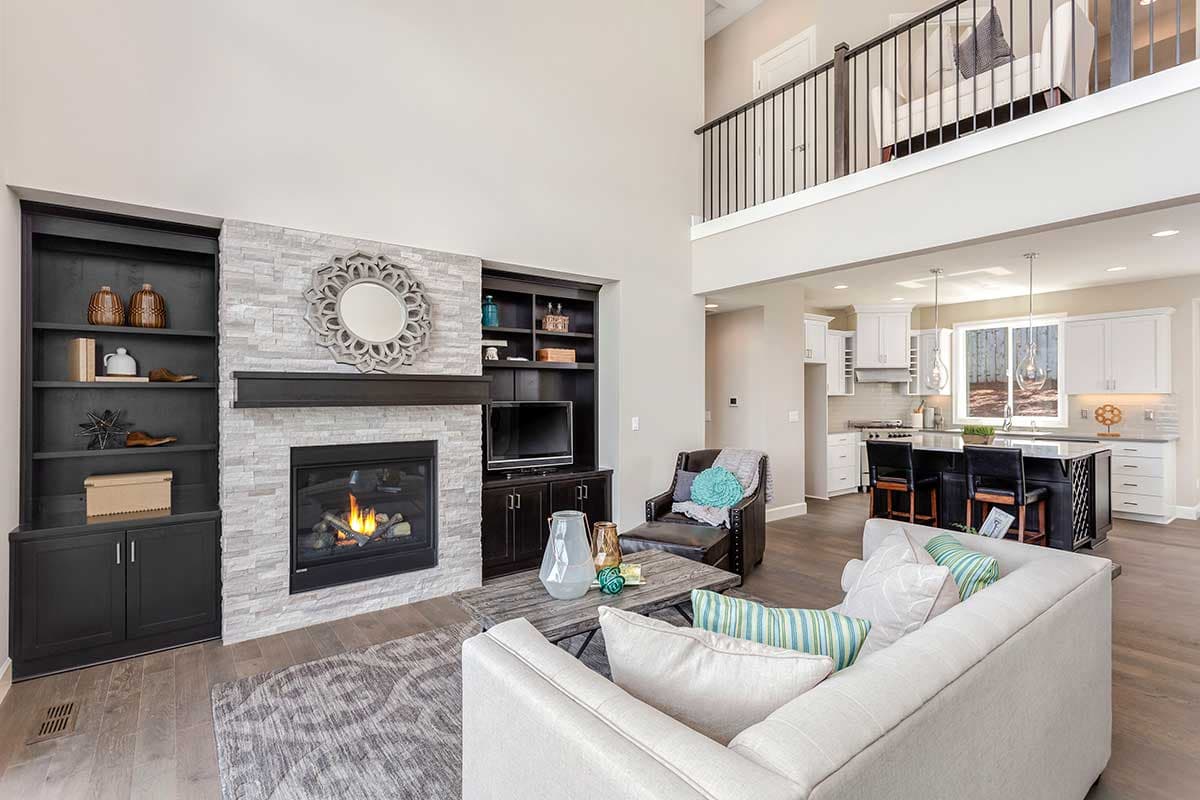 Great room with two-story ceiling, stone fireplace, built-in shelving, and open-concept kitchen with island.
