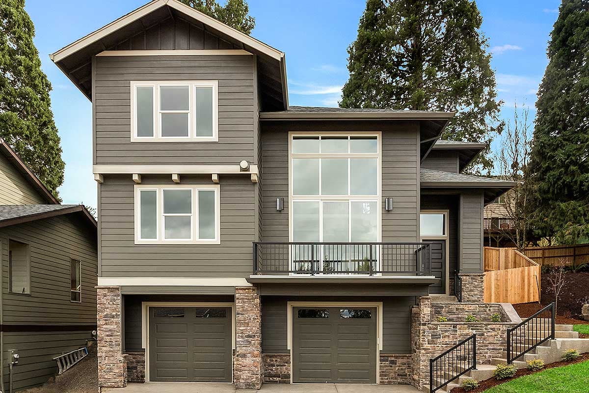 Modern house plan exterior: three stories, dark siding, stone base, multiple gables, large windows, and a balcony.