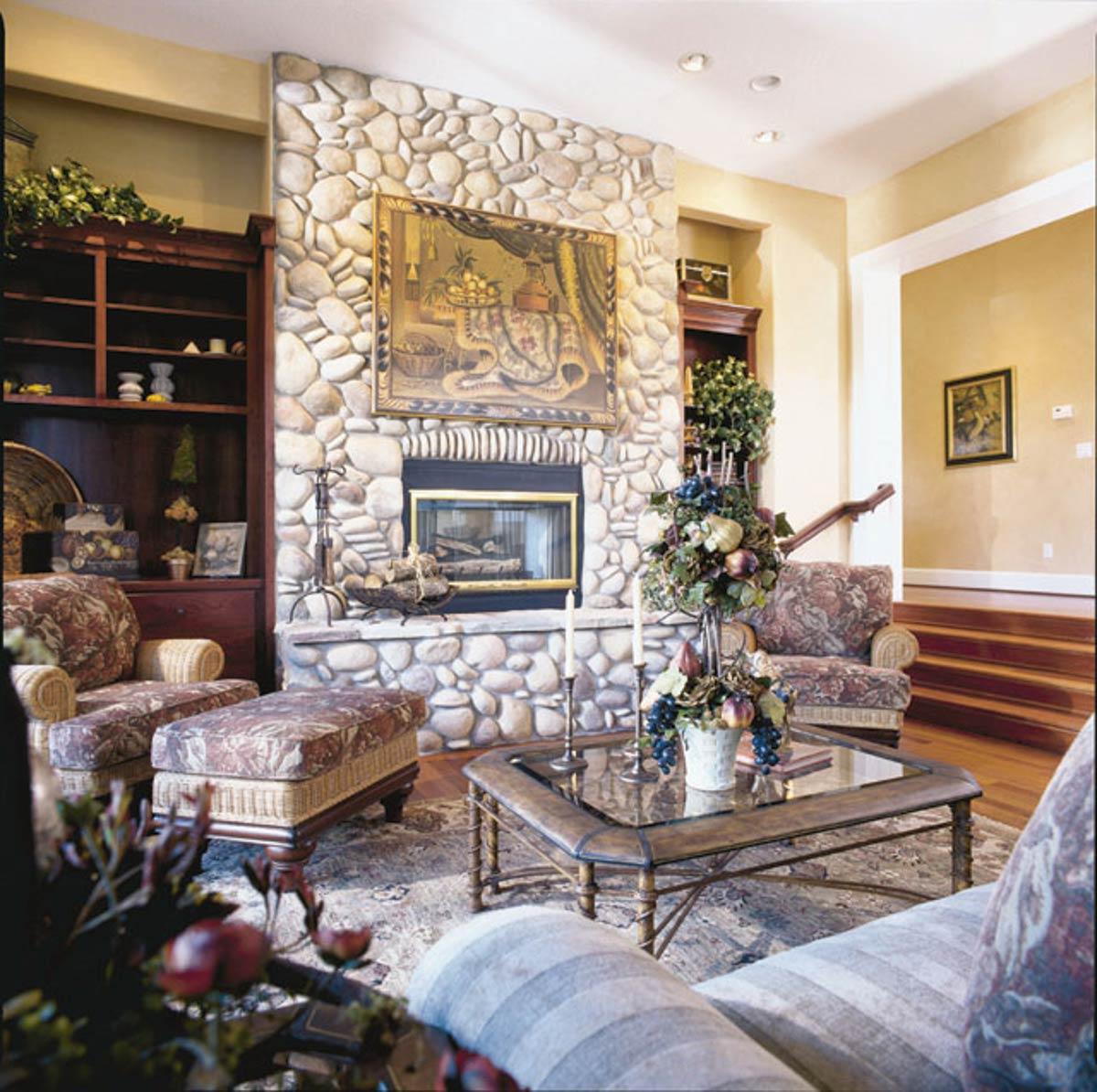 Living room featuring a large stone fireplace with a mosaic above, built-in bookshelves, and seating.