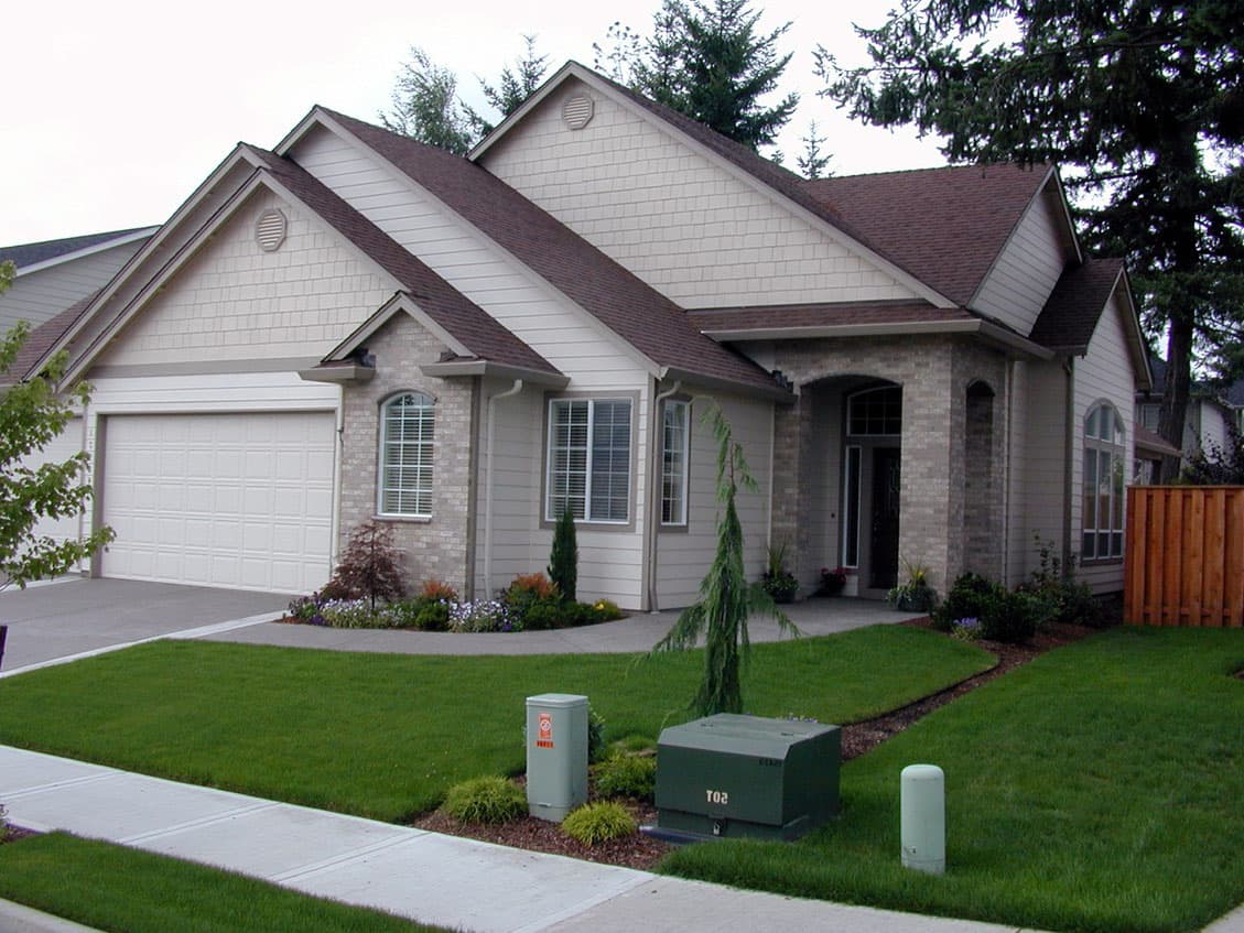 House plan exterior showing a one-story home with an attached garage, arched entryway, and stacked gable rooflines.