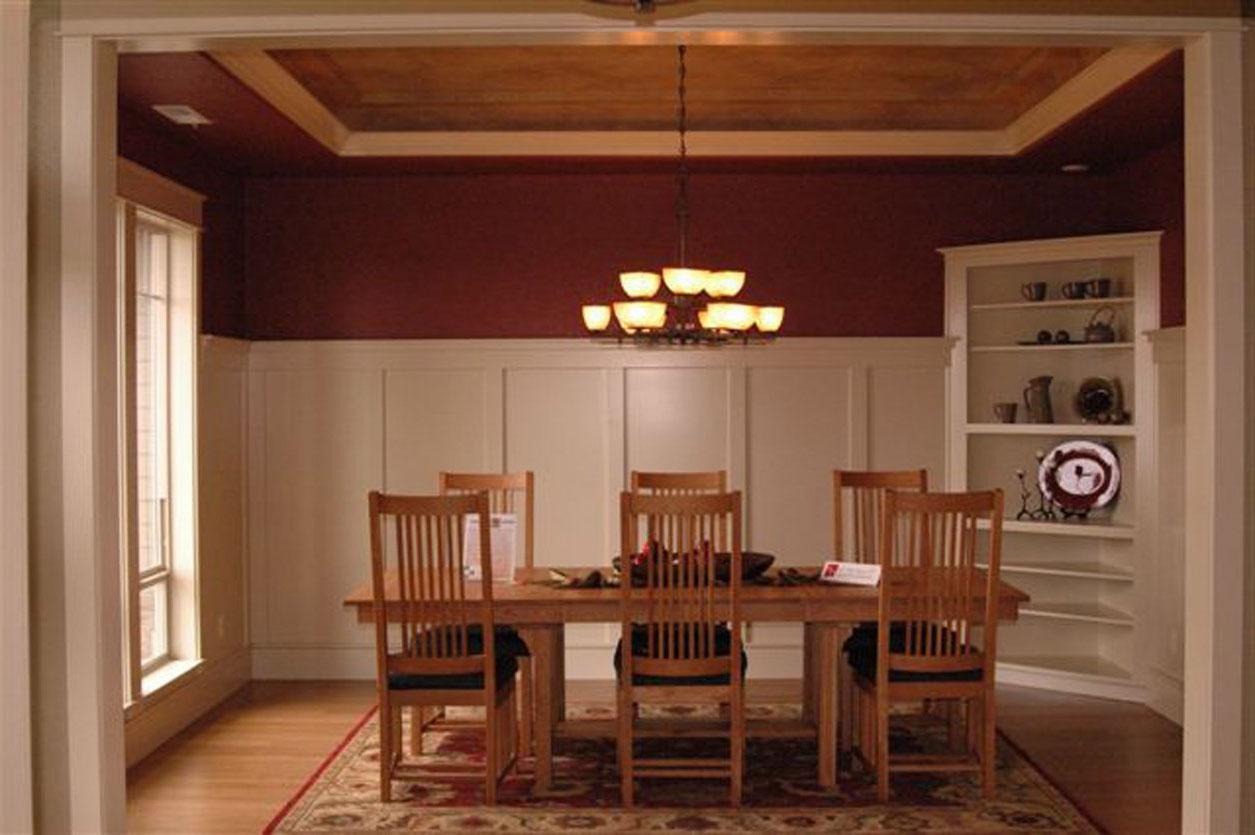 Dining room with wood table, chairs, coffered ceiling, wainscoting, and built-in shelving.