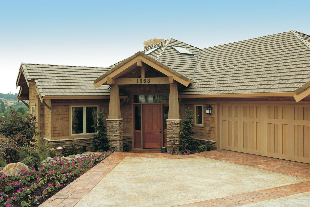 House plan exterior featuring a covered entry with stone pillars, a wooden garage door, and a shingled roof.