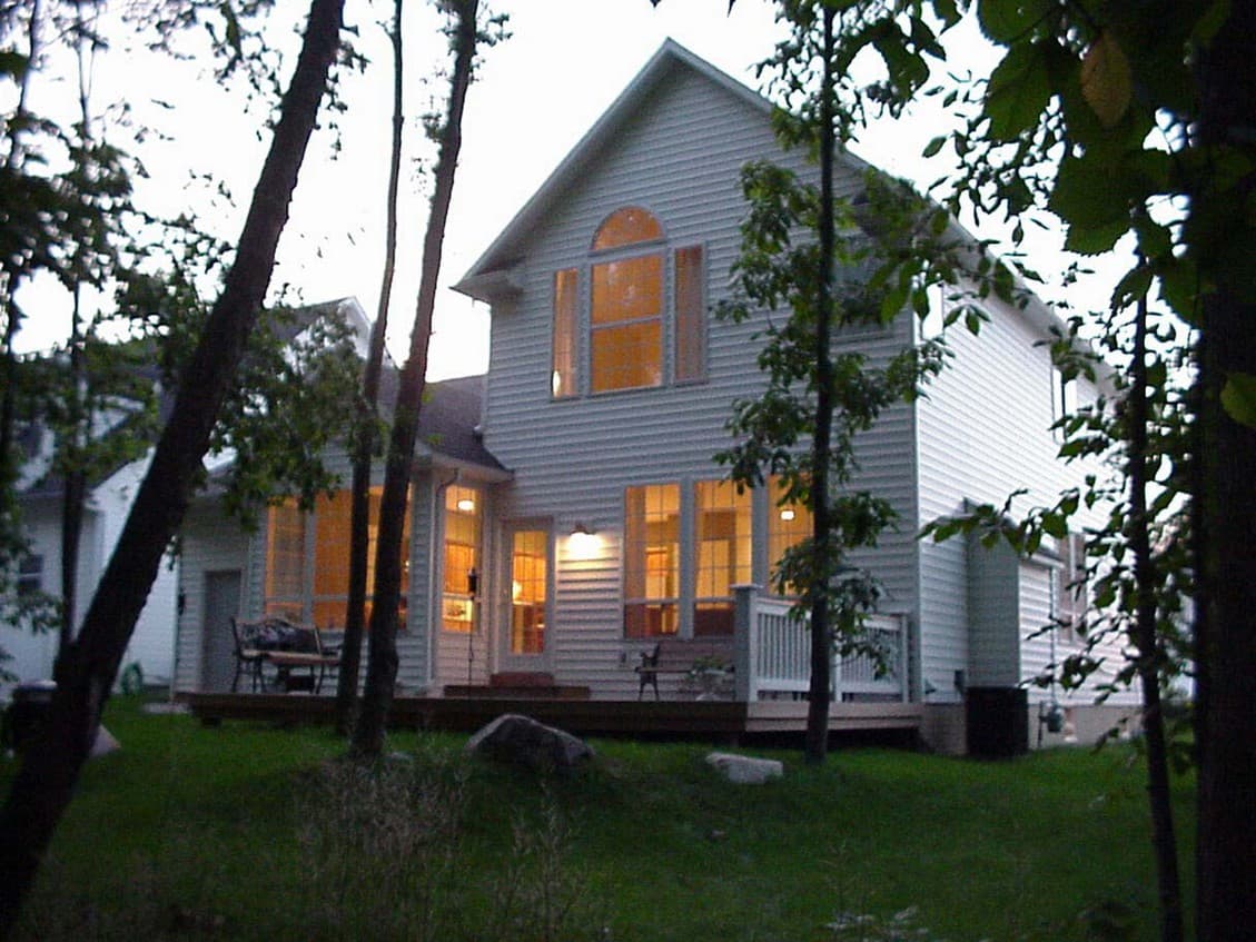 House plan exterior: Two-story siding home with gable roof, arched upper window, and deck with railing.