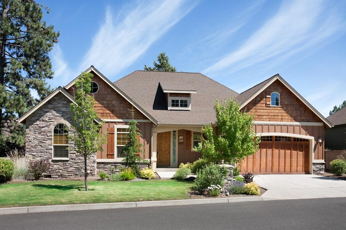 House plan exterior: One-story home with stone and wood siding, arched windows, dormer, and wood garage door.