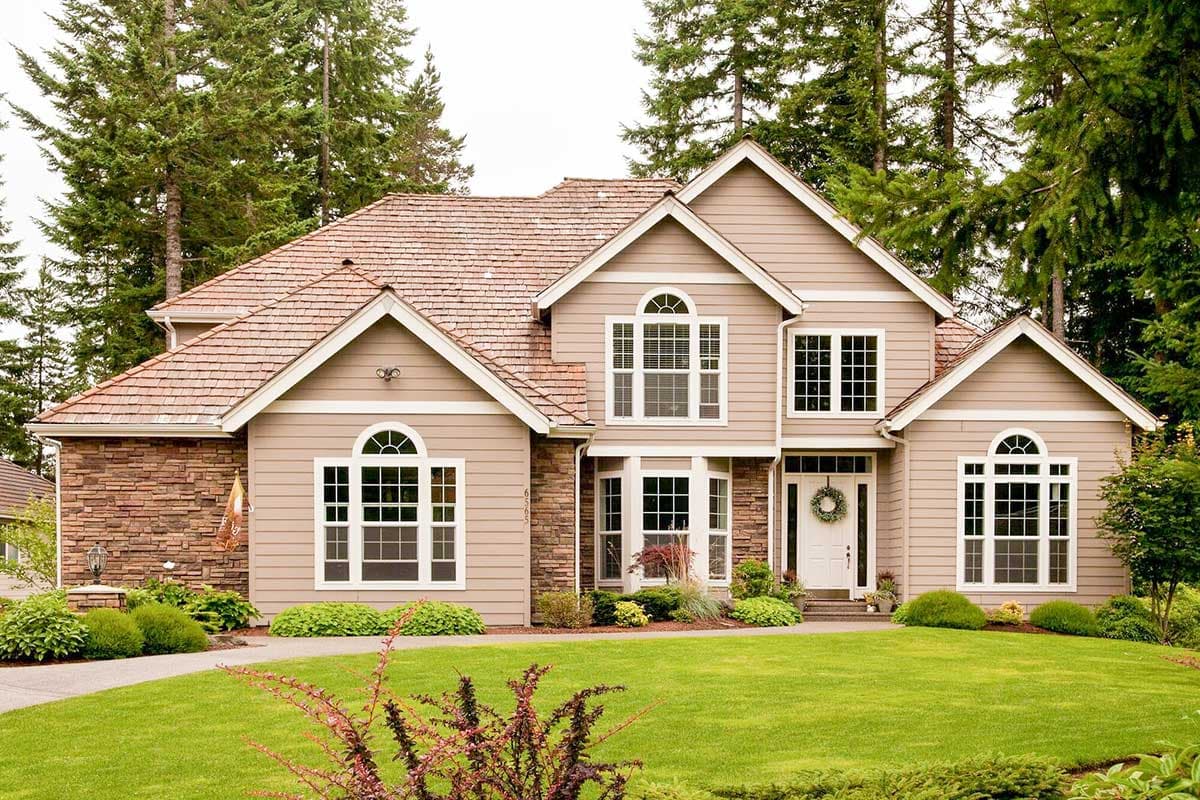 House plan exterior. Two-story home with a gabled roof, stone accents, and multiple arched windows. Front porch and a circular drive.