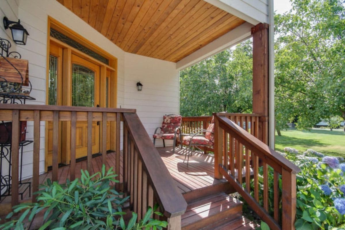 Front porch with wooden steps, railing, and tongue-and-groove ceiling leading to a double door entry.