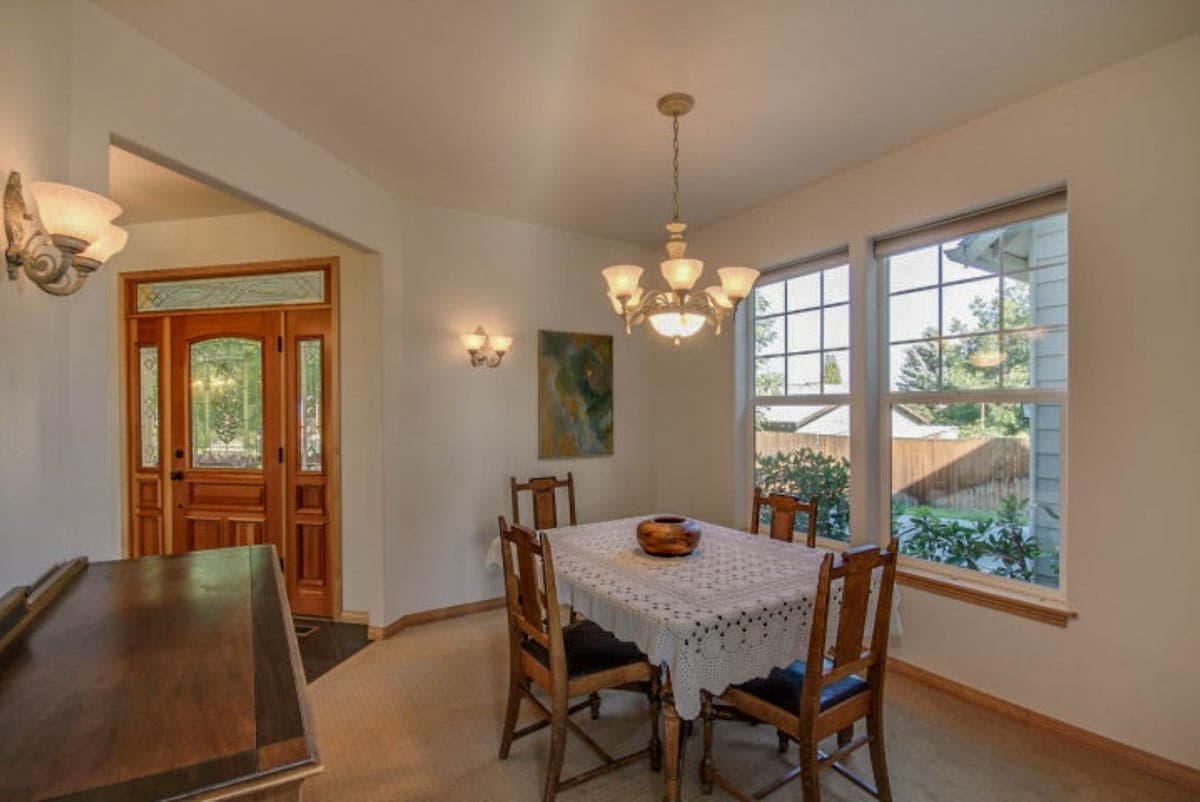 Dining room with wood door, chandelier, large windows, and dining table set for four.