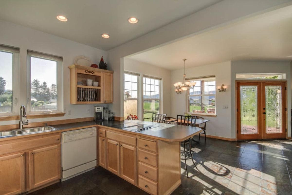 Kitchen with island, dining area, and double entry doors with decorative glass. Includes sink, dishwasher, and ample cabinetry.