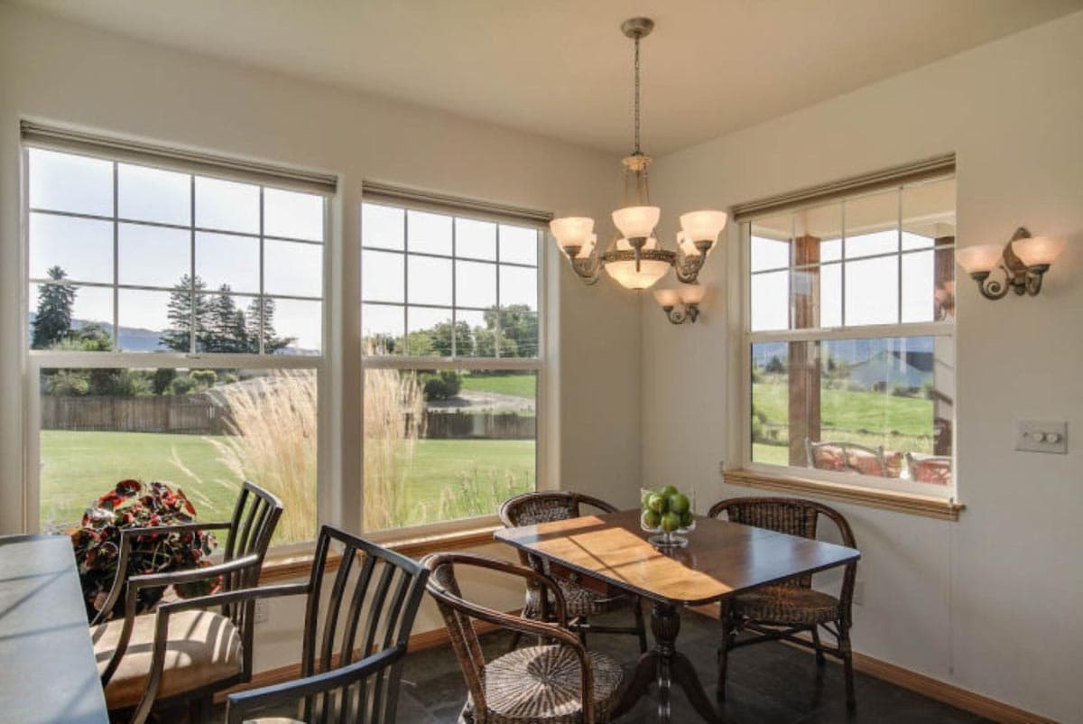 Dining area with a table, chairs, chandelier, and large windows with a view of a grassy yard and trees.