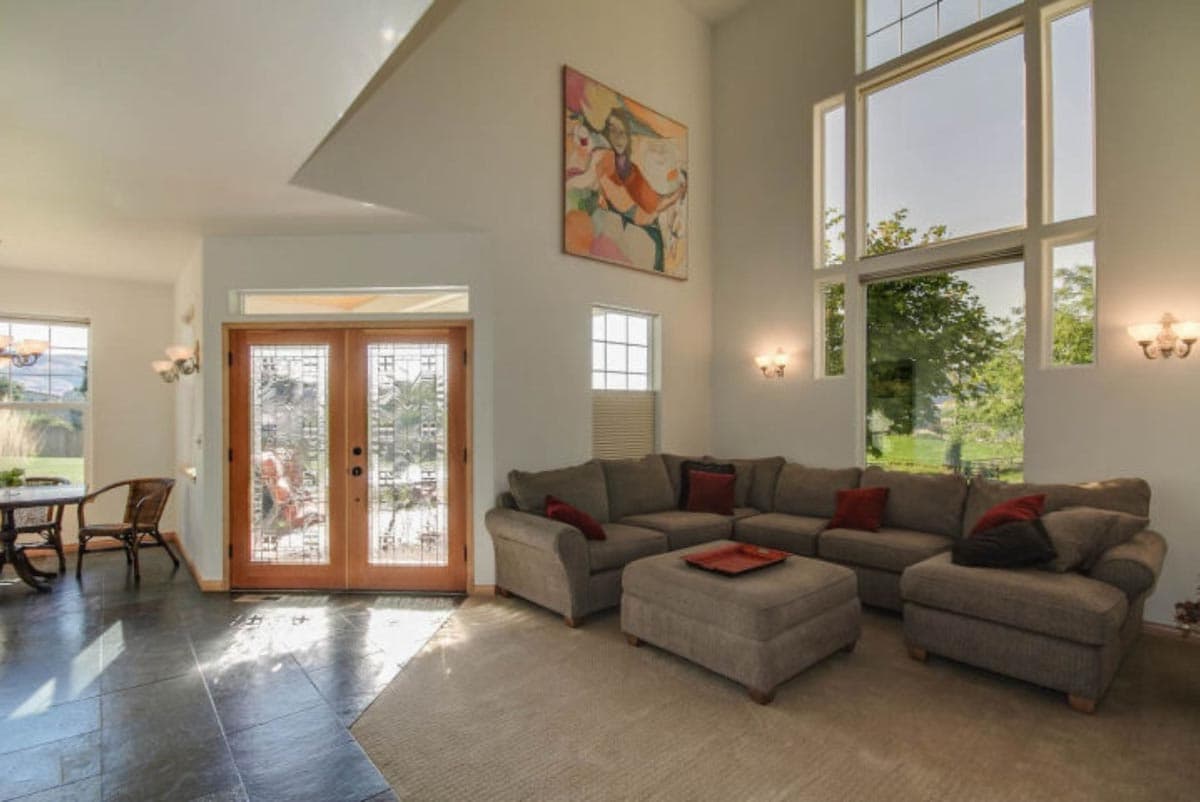 Living room with large sectional sofa, double entry doors with decorative glass, and floor-to-ceiling windows.