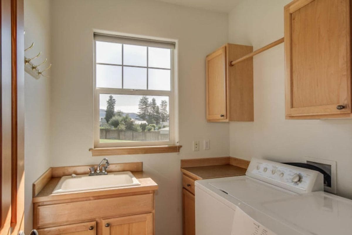 Laundry room with sink, washer, wood cabinets, and a drying rod.