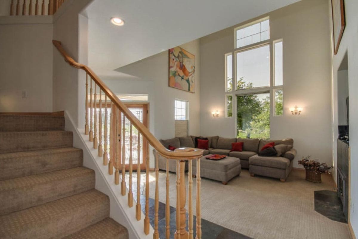 Interior view of great room with a carpeted staircase, sectional sofa, and a large wall of windows.