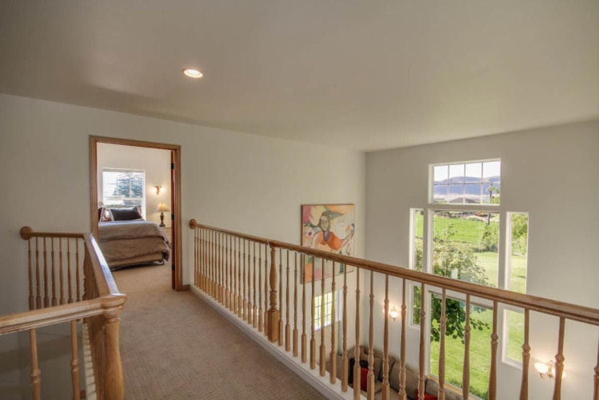 Interior hallway overlooks bedroom and views of green landscape through multiple windows.