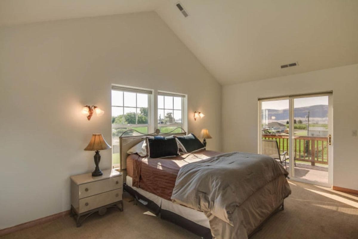 Bedroom with vaulted ceiling, two windows, and sliding glass door to deck.
